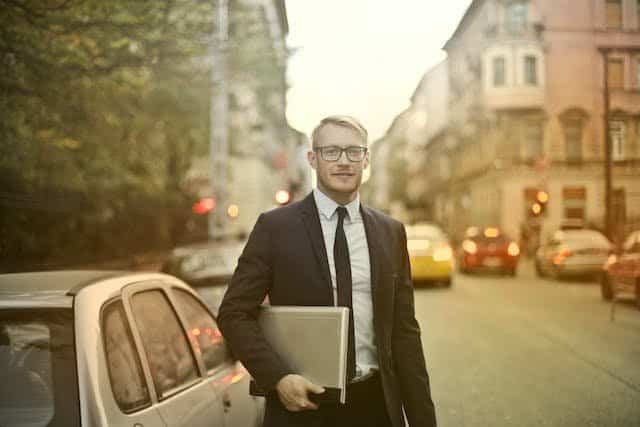 A businessman in a suit walking down the street with a laptop.