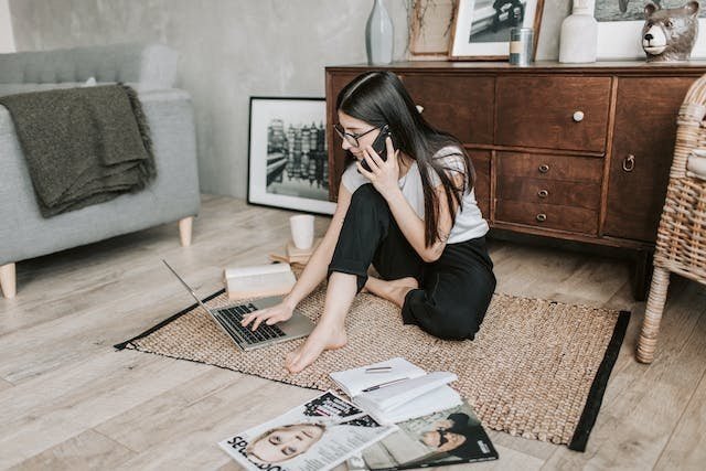 Asian woman sitting on the floor with a laptop in her living room.