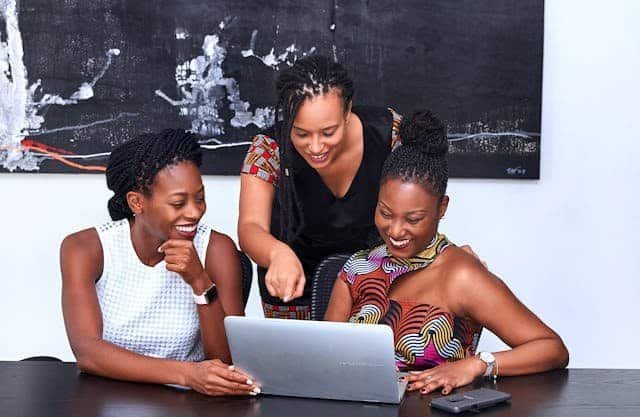 Three women sitting around a table looking at a laptop.