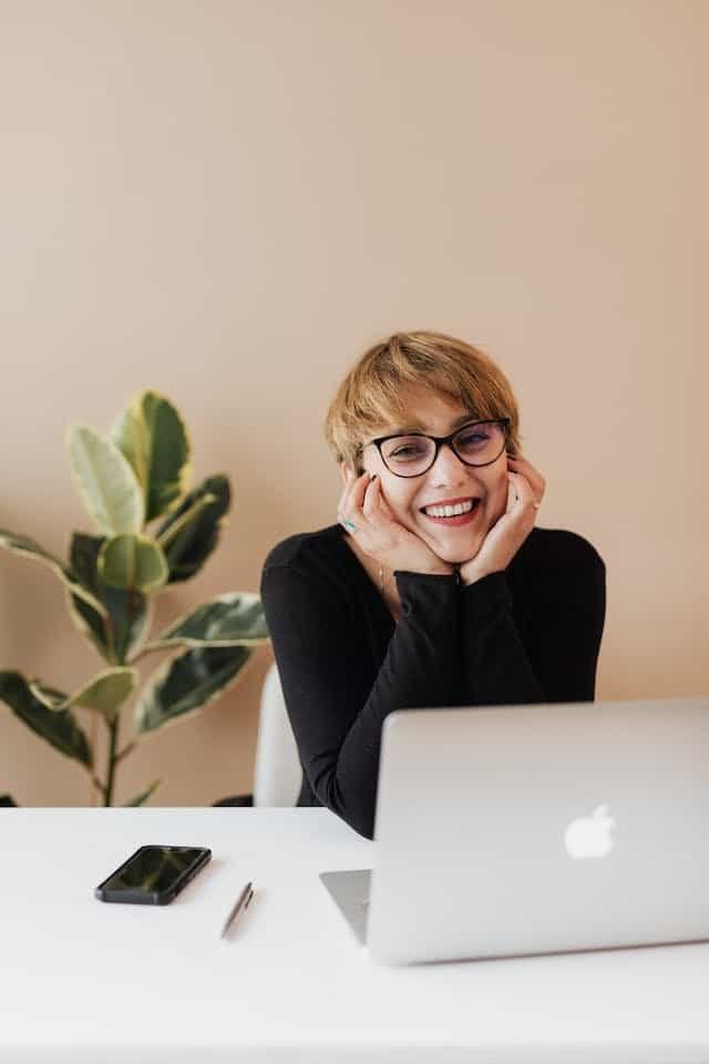 A smiling woman sitting at a desk with a laptop.