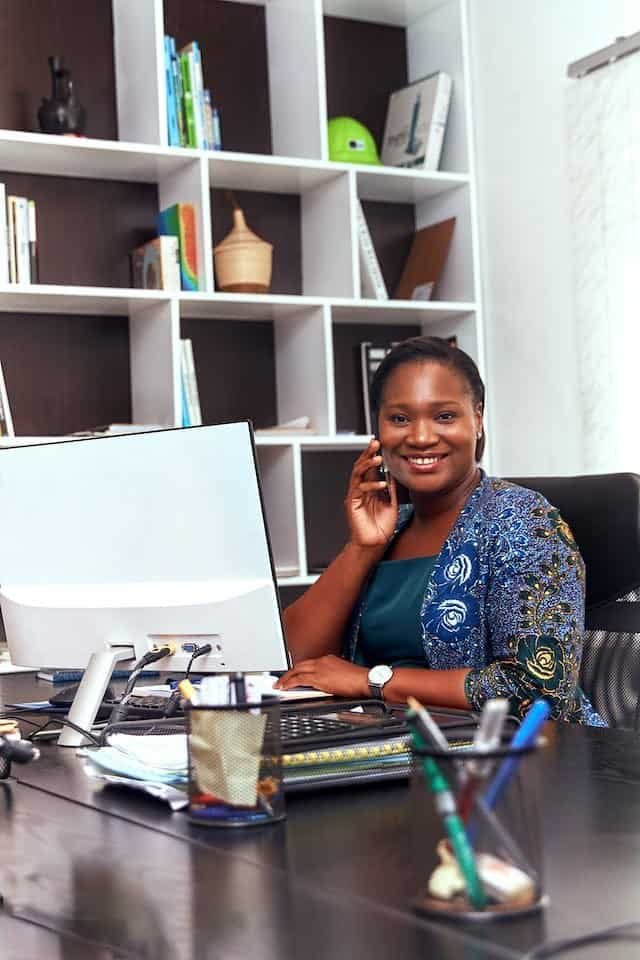 A young african woman sitting at a desk and talking on the phone.