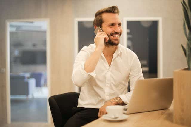 A man is talking on the phone while sitting at a desk.