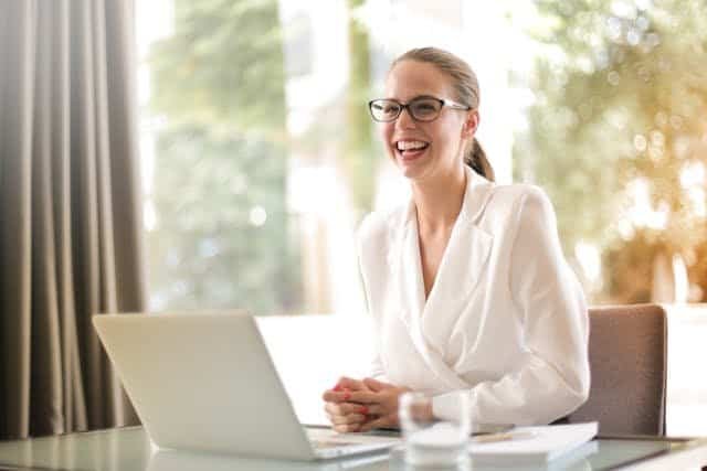 A smiling business woman sitting at a desk with a laptop.