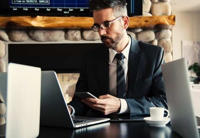 A businessman sitting at a desk with a laptop and cell phone.