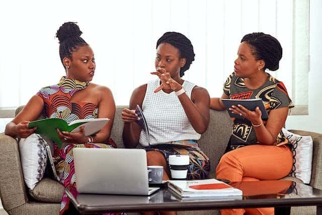 Three african women sitting on a couch with laptops.