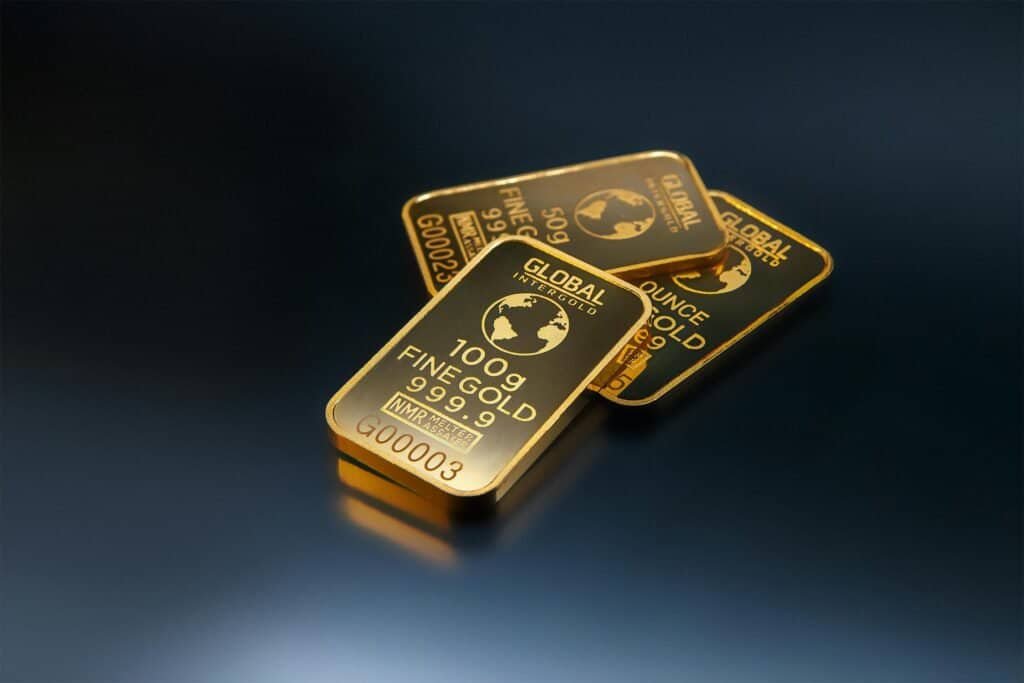 Three gold bars on a black surface attract savvy investors looking into buying gold.